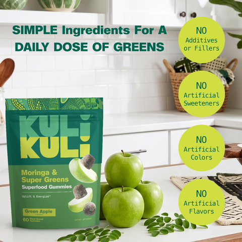 Kuli Kuli Moringa & Super Greens gummies pouch on a white kitchen counter with green apples and moringa sprigs, beside badges reading no additives or fillers, no artificial sweeteners, no artificial colors, and no artificial flavors.